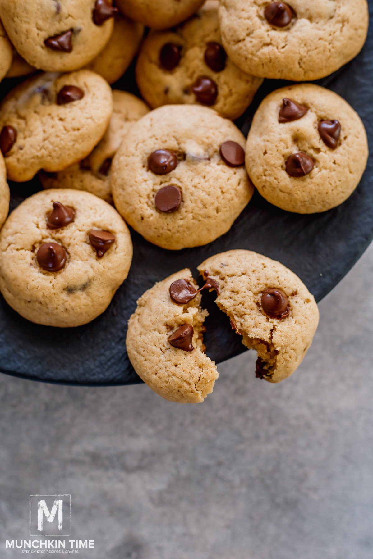 Soft Chocolate Chip Cookies on a plate with one cookie broken in half with melted chocolate pull.