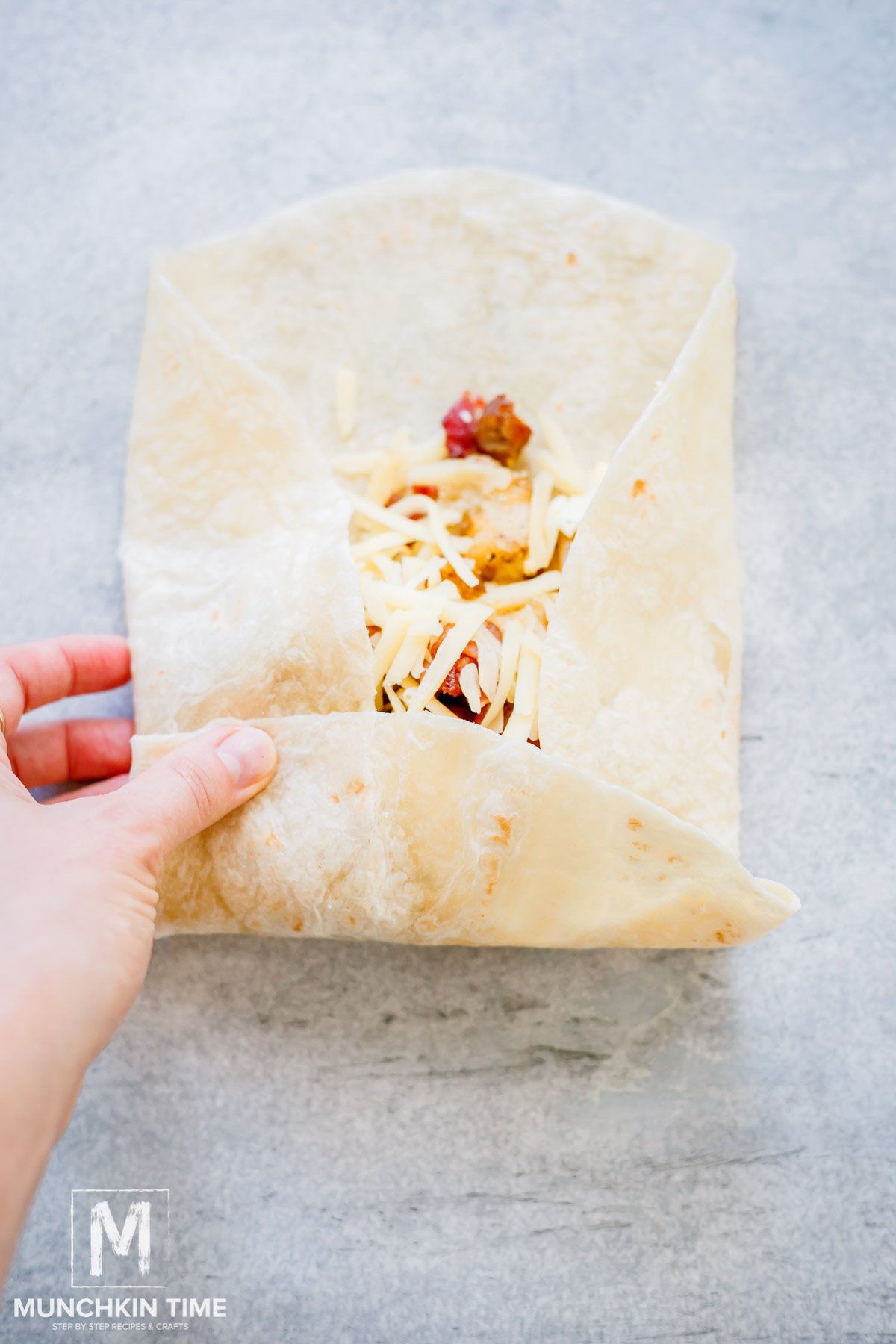 folding large tortilla with filling into burrito.