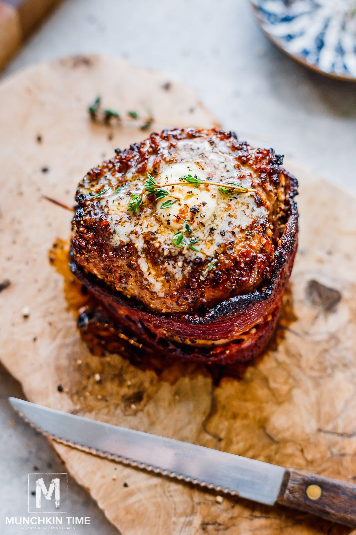 Bacon Wrapped Filet Mignon on a cutting plate with butter and thyme.