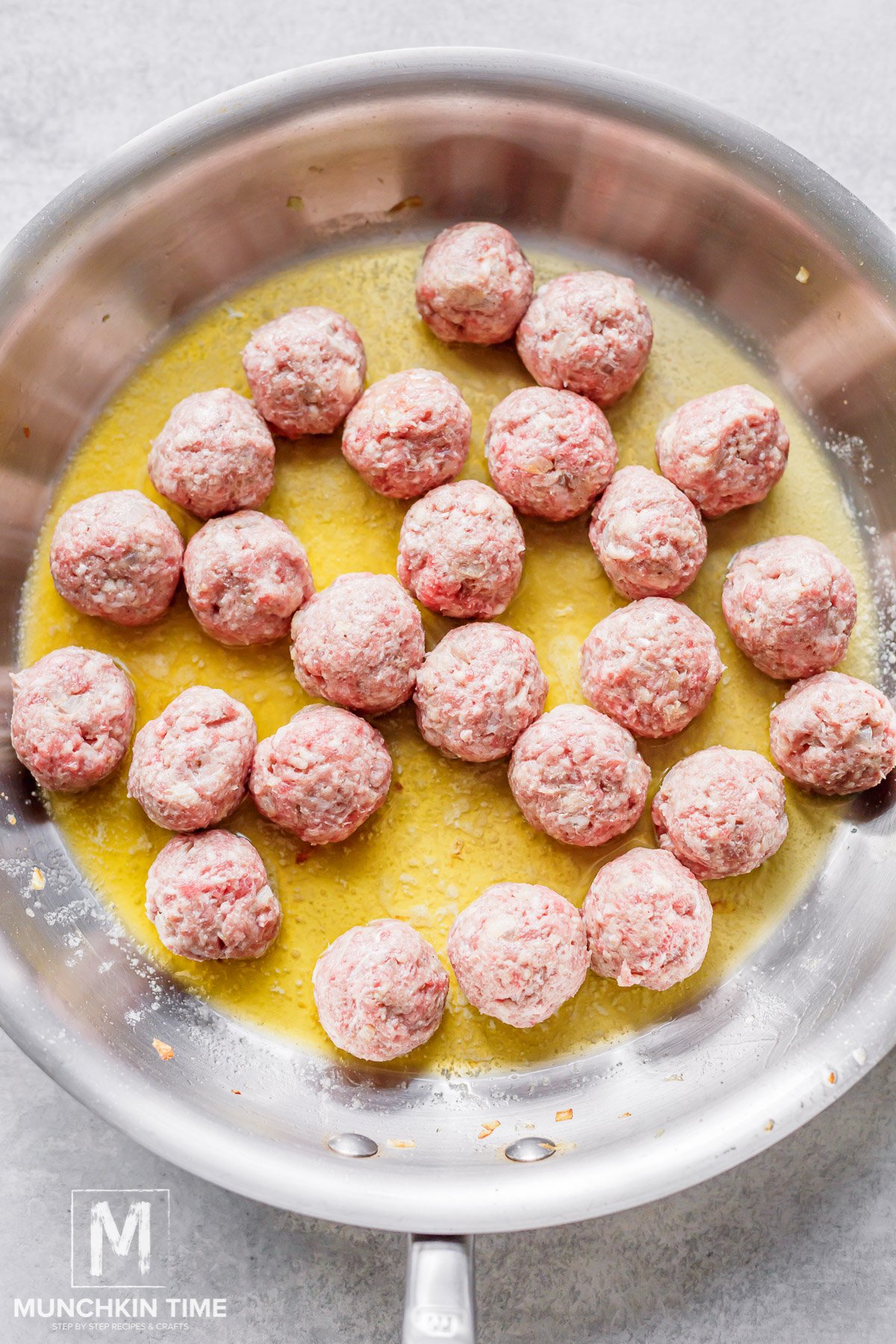 raw meatballs cooking in the skillet with butter.